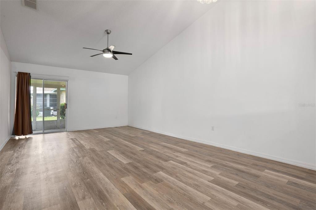 An empty living room features wood-look flooring, a vaulted ceiling, and a sliding glass door — 3200 VILLA WAY CIRCLE, ST CLOUD, FL