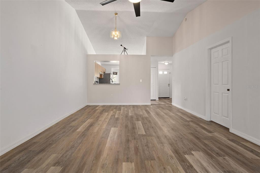 A living room with vaulted ceilings, wood-look flooring, and a kitchen pass-through window — 3200 VILLA WAY CIRCLE, ST CLOUD, FL
