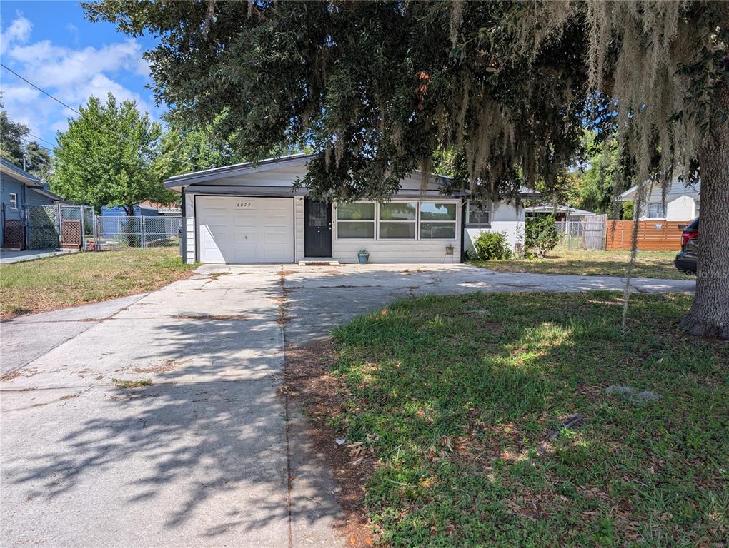 A single-story house with a white garage, dark front door, and a large tree in front — 4079 LAKE MARIANNA DRIVE, WINTER HAVEN, FL