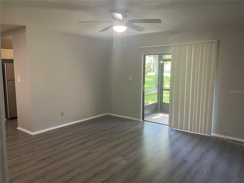 An empty living room features gray walls, dark wood-look flooring, a ceiling fan, and sliding doors — 134 SPRINGWOOD CIRCLE UNIT B, LONGWOOD, FL