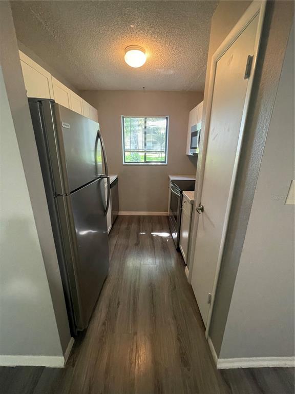 A galley-style kitchen features stainless steel appliances, white cabinetry, and wood-look flooring — 134 SPRINGWOOD CIRCLE UNIT B, LONGWOOD, FL