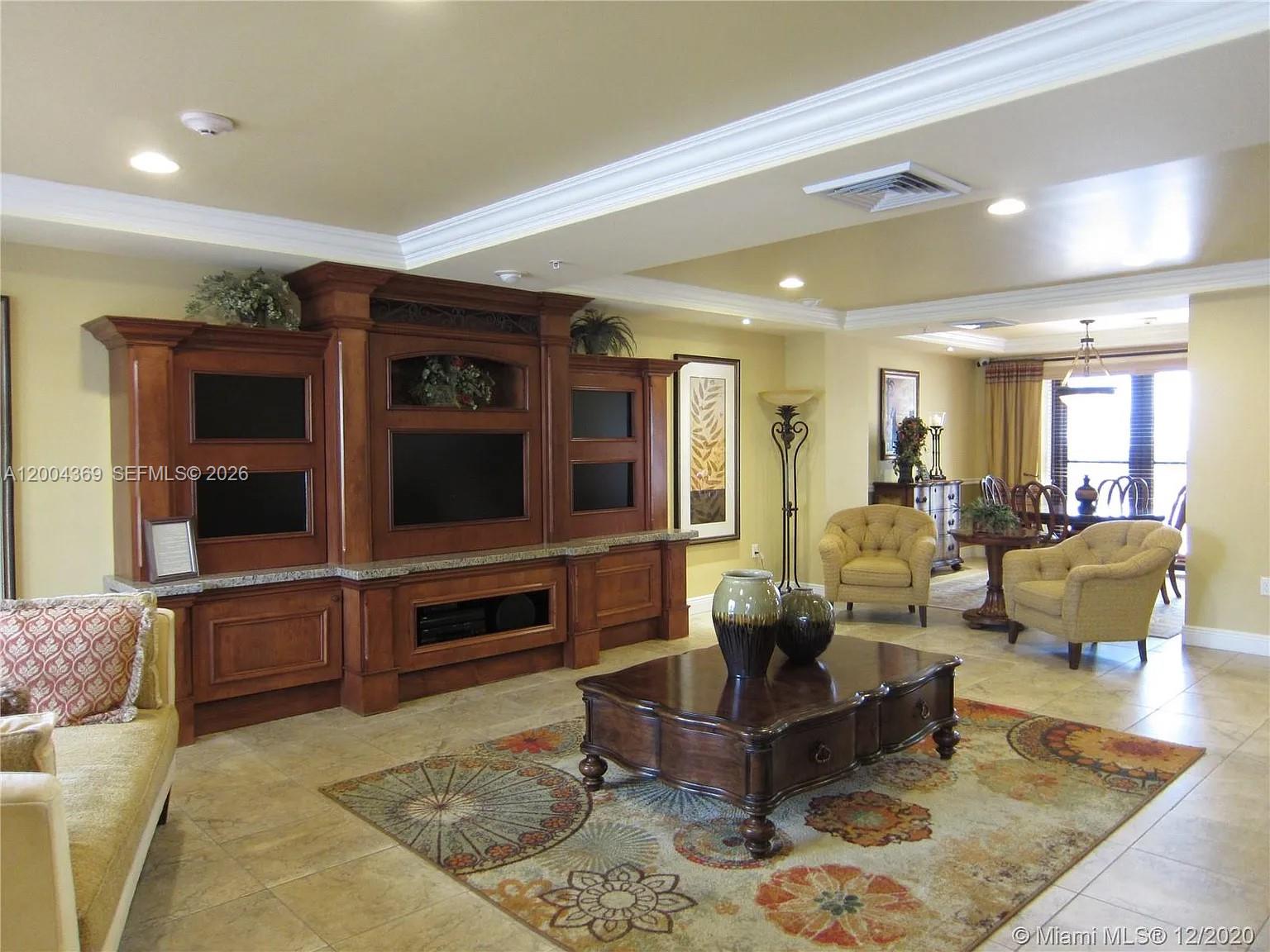 A living room features a large wooden entertainment center, tile floors, and a patterned area rug — 888 S Douglas Rd # 1512, Coral Gables FL 33134, CORAL GABLES, FL