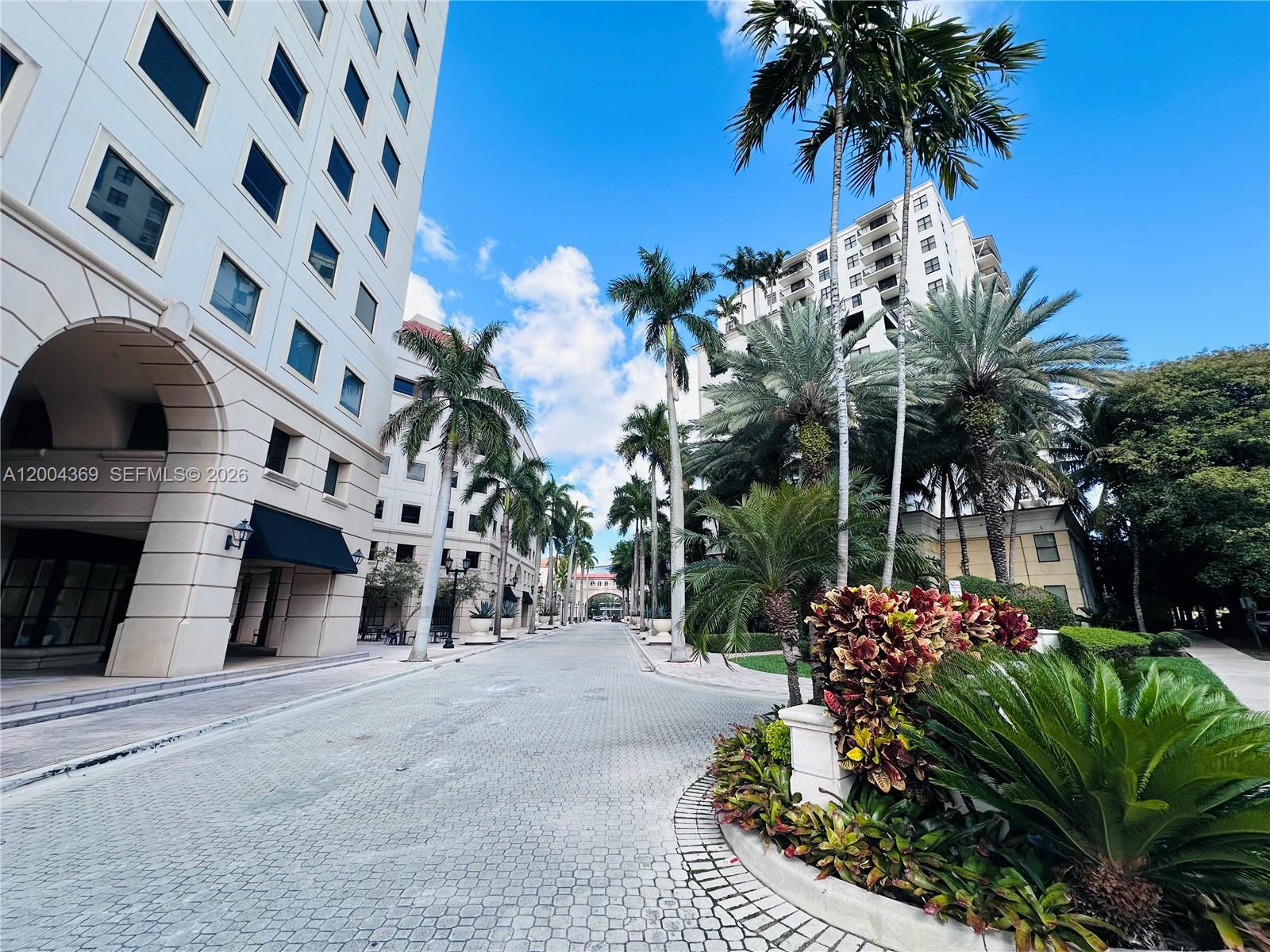 A paved street lined with palm trees and large buildings under a blue sky — 888 S Douglas Rd # 1512, Coral Gables FL 33134, CORAL GABLES, FL