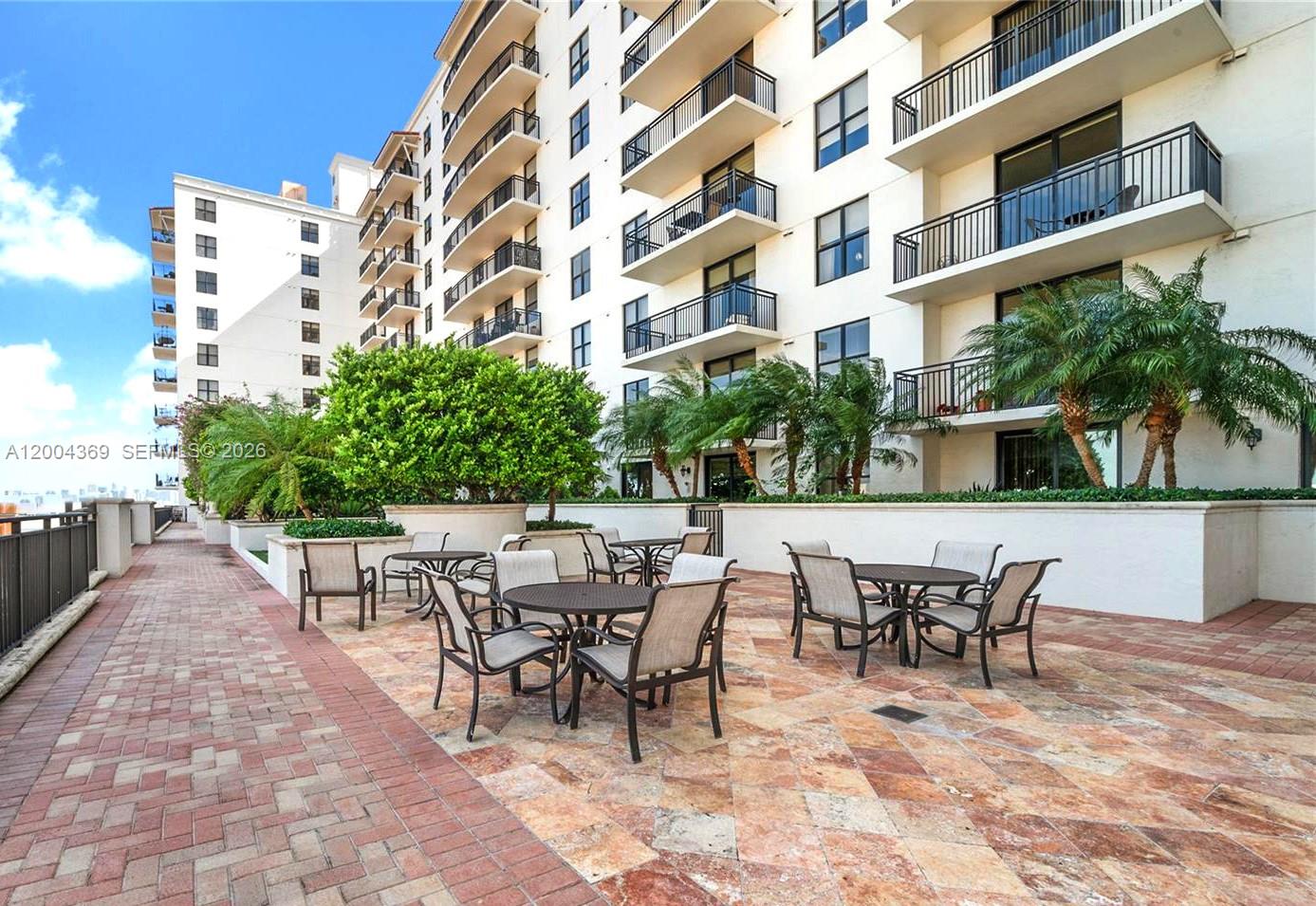 An outdoor patio area features tables and chairs on a stone-tiled terrace by a building — 888 S Douglas Rd # 1512, Coral Gables FL 33134, CORAL GABLES, FL