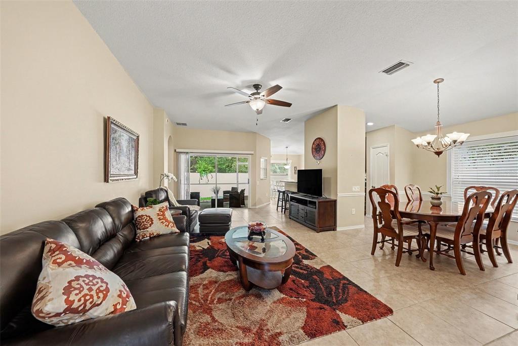 A living and dining room features tile floors, a dark leather sofa, and a rug — 26351 WHIRLAWAY TERRACE, WESLEY CHAPEL, FL