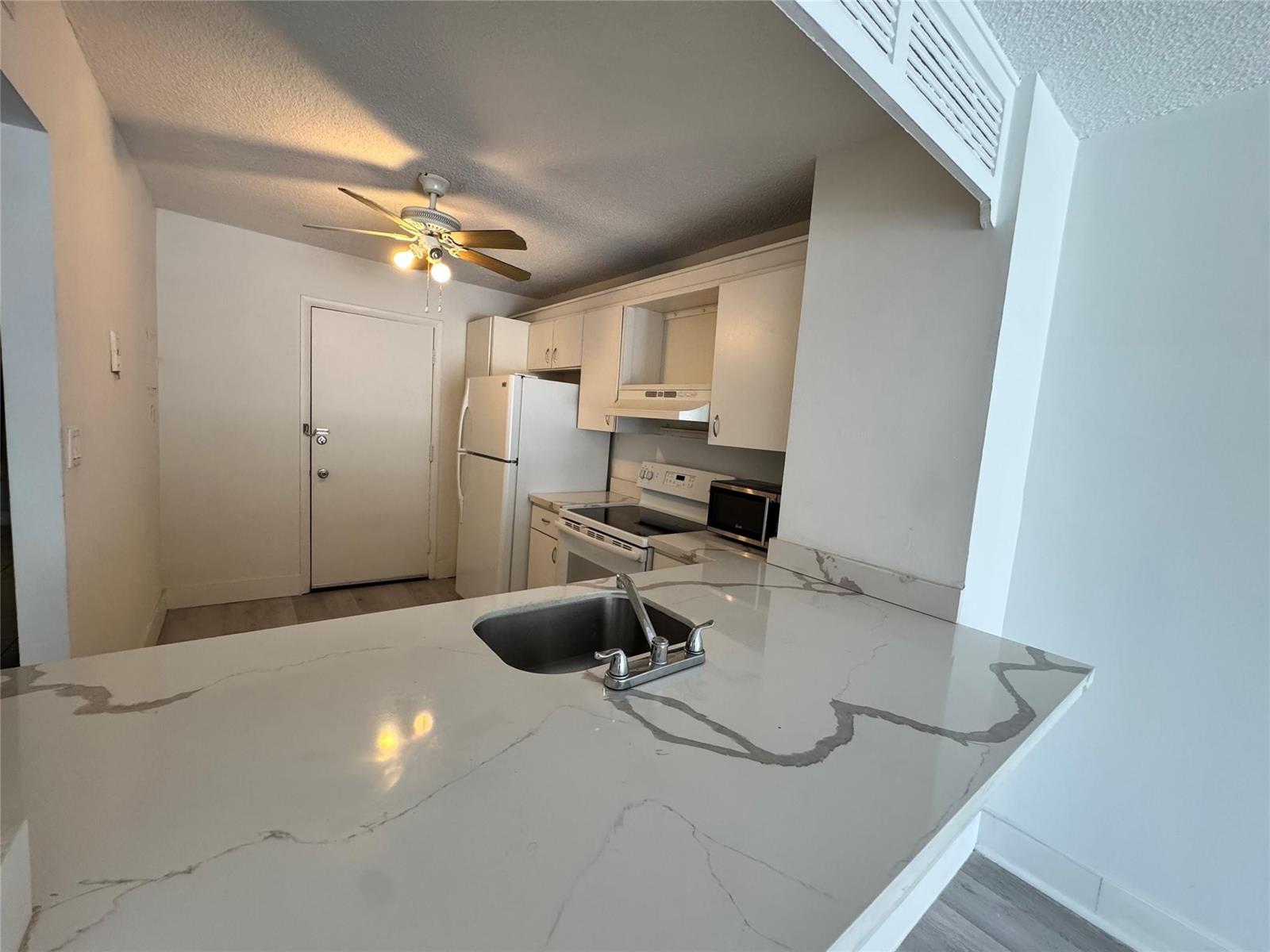 A kitchen features white cabinets, a white refrigerator, a stove, and a marble-patterned countertop — 6855 Abbott Avenue # 201, Miami Beach FL 33141, MIAMI BEACH, FL