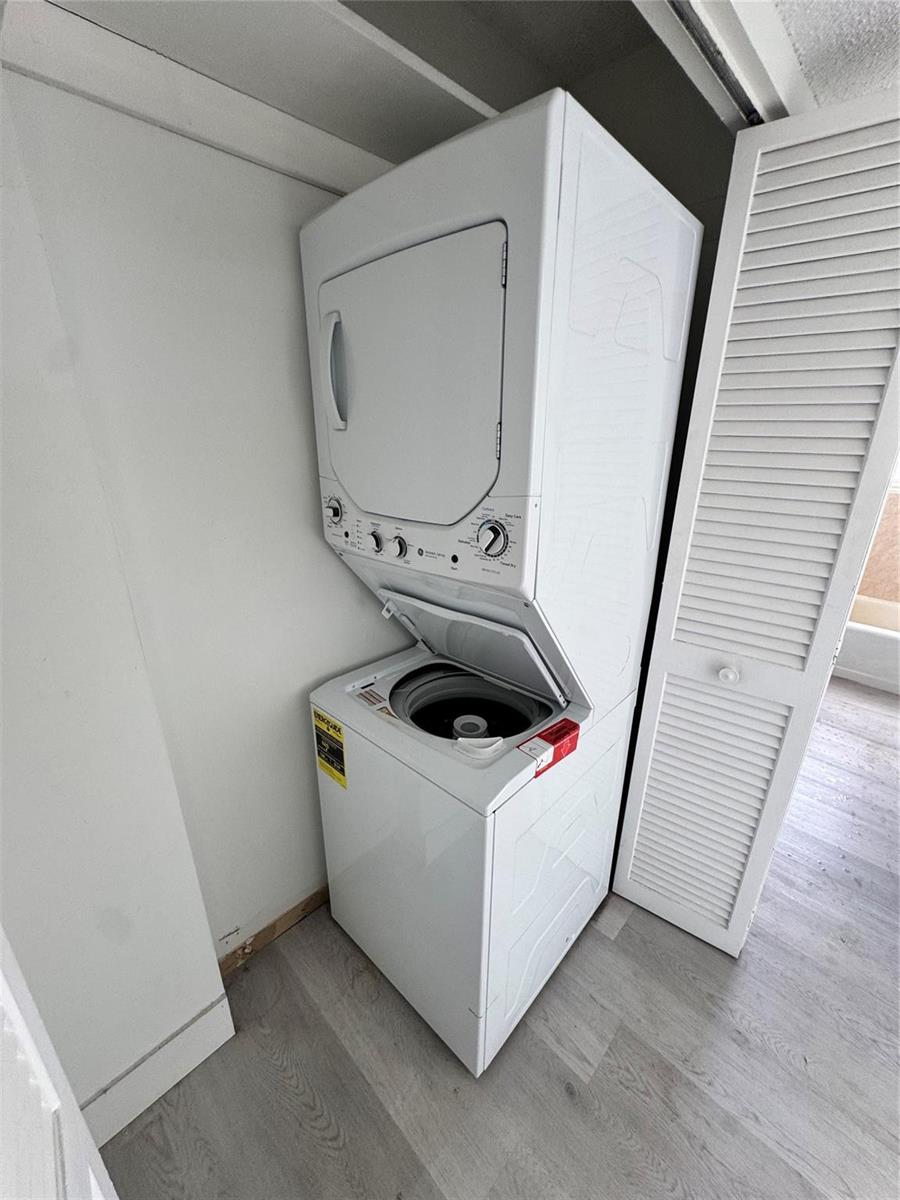 A white stacked washer and dryer unit sits in a closet with light wood flooring — 6855 Abbott Avenue # 201, Miami Beach FL 33141, MIAMI BEACH, FL