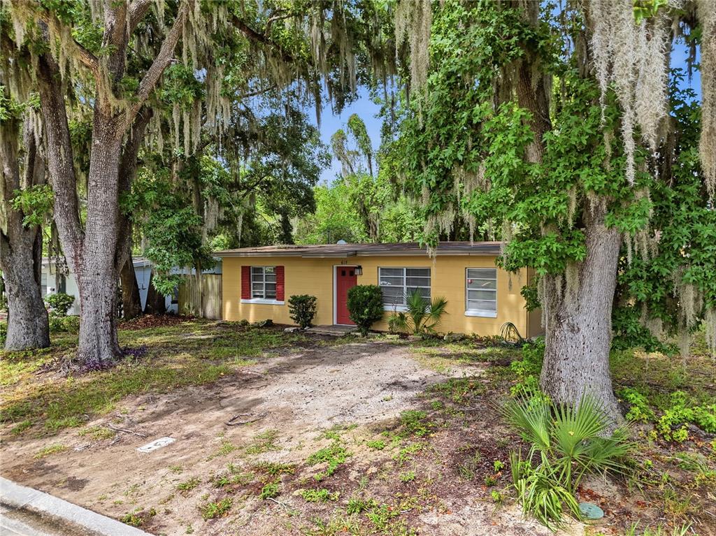 A yellow single-story house with a red door sits among trees with hanging moss — 615 DANVERS STREET, EUSTIS, FL