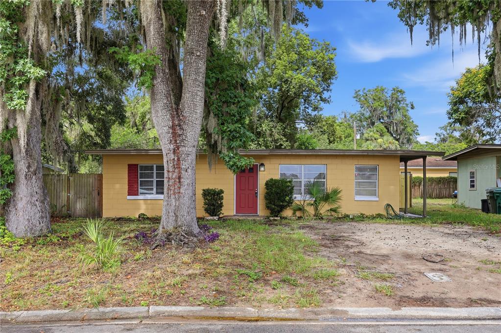 A single-story yellow concrete block house with a red front door and a large tree — 615 DANVERS STREET, EUSTIS, FL