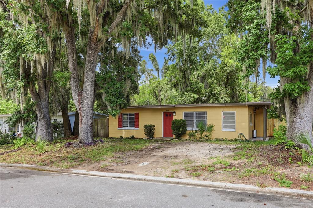 A single-story yellow house with a red front door sits under large mossy trees — 615 DANVERS STREET, EUSTIS, FL