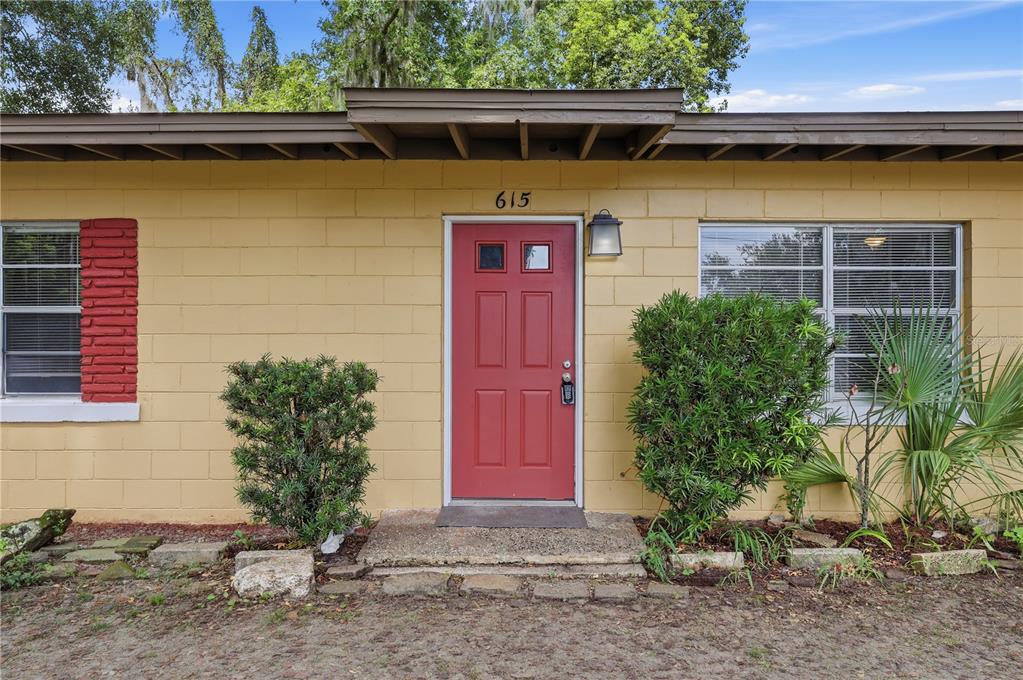 A yellow concrete block house features a red front door and two windows — 615 DANVERS STREET, EUSTIS, FL