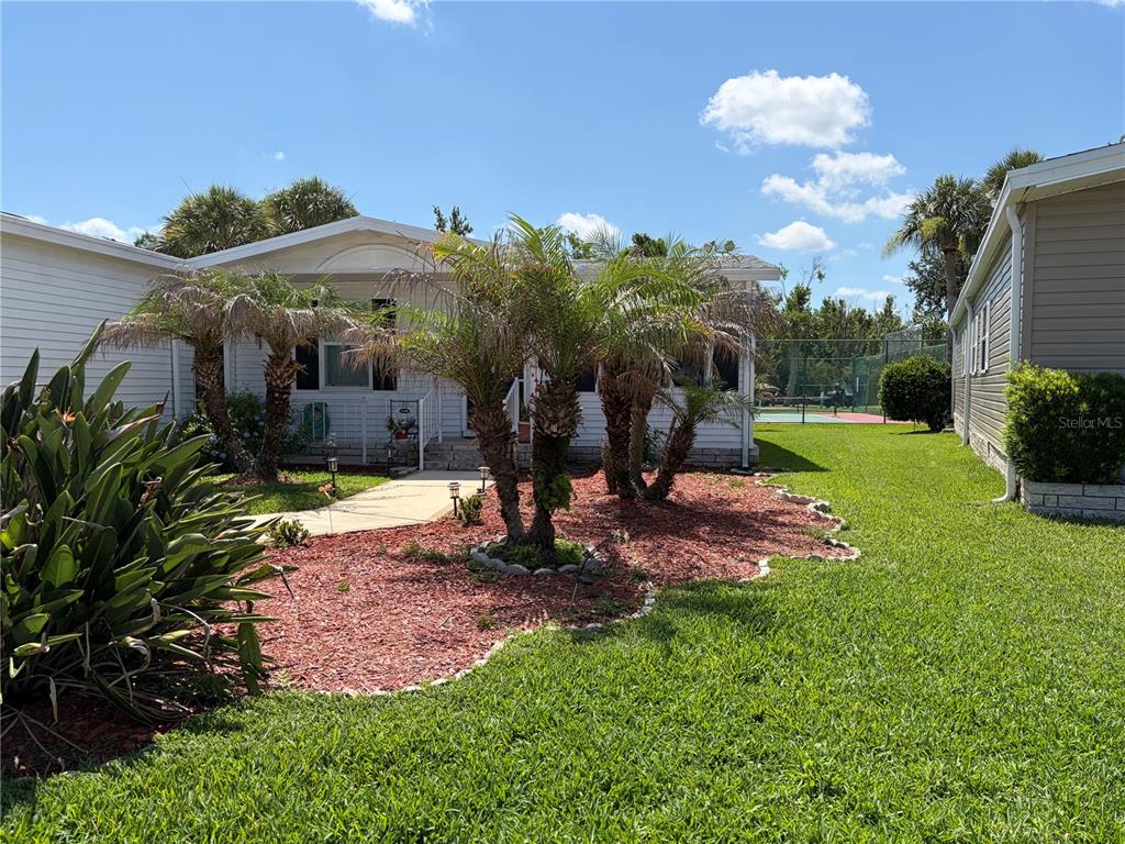 A white manufactured home features a landscaped front yard with palm trees and red mulch — 144 VICTORIA DRIVE, HAINES CITY, FL