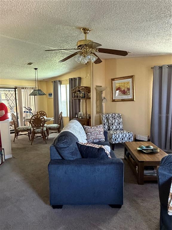 A living room with a blue sofa, patterned accent chair, and an adjacent dining area — 144 VICTORIA DRIVE, HAINES CITY, FL