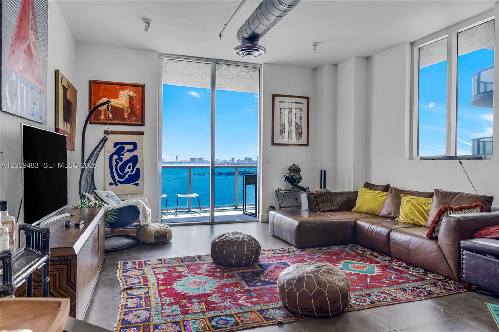 A living room features a brown leather sectional, a colorful rug, and a balcony view — 700 NE 25th St # 1104, Miami FL 33137, MIAMI, FL