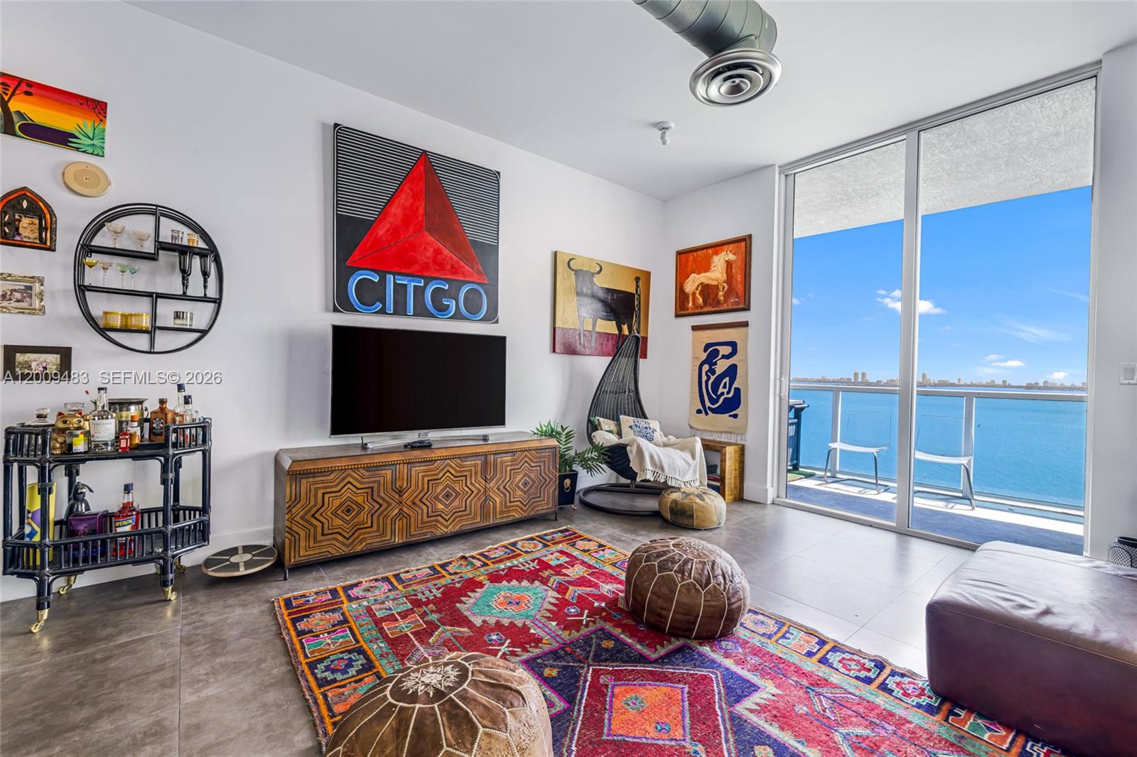 A living room features a patterned rug, a Citgo sign, and a balcony overlooking water — 700 NE 25th St # 1104, Miami FL 33137, MIAMI, FL
