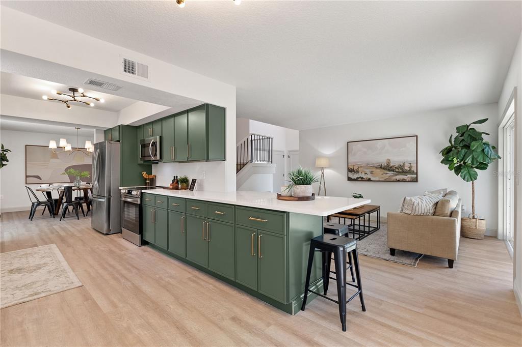 A modern kitchen with green cabinets and a white island overlooks an open living area — 3906 BLOOMING HILL LANE, PALM HARBOR, FL