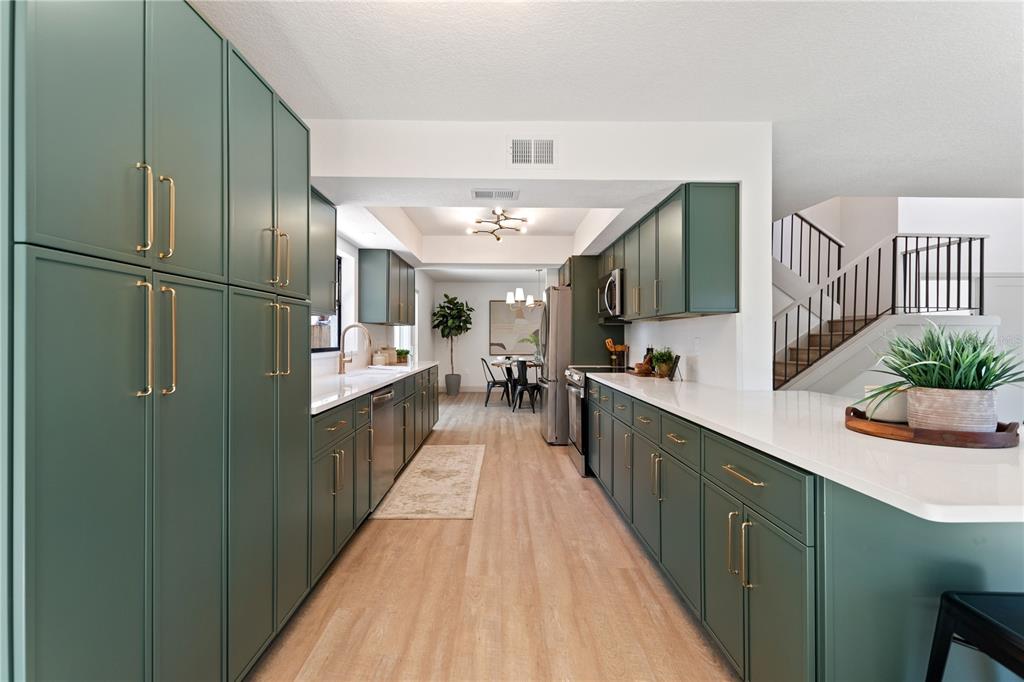 A kitchen features green cabinets, gold hardware, white countertops, and light wood-look flooring — 3906 BLOOMING HILL LANE, PALM HARBOR, FL
