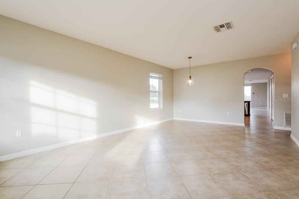 An empty room with beige walls, tile flooring, a single pendant light, and an arched doorway — 3627 RYEGRASS STREET, CLERMONT, FL
