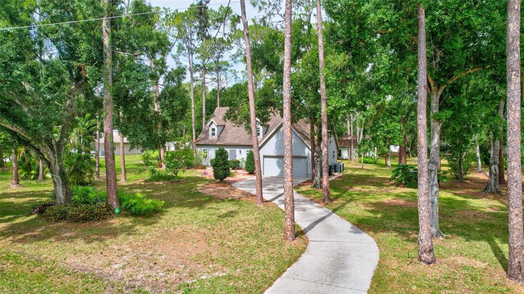 A two-story house with a gray exterior and a concrete driveway sits among many trees — 9607 OAK RUN DRIVE, BRADENTON, FL