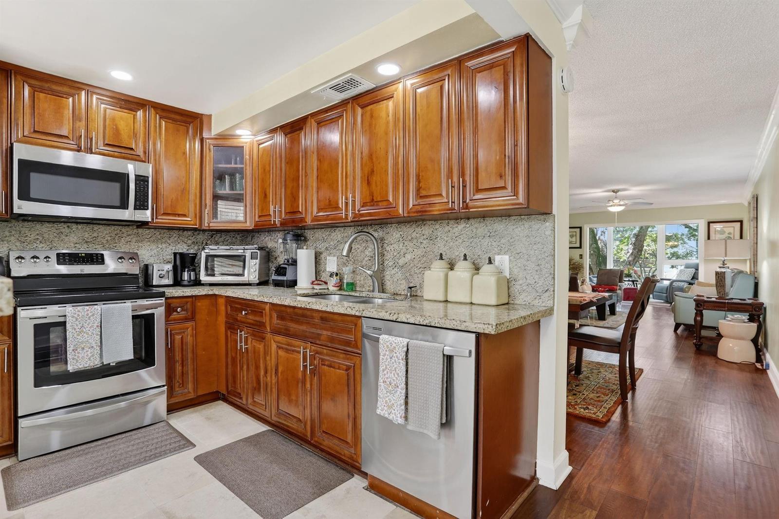 A kitchen with wood cabinets, granite countertops, and stainless steel appliances opens to a living area — 2403 Antigua Circle # B2, Coconut Creek FL 33066, COCONUT CREEK, FL