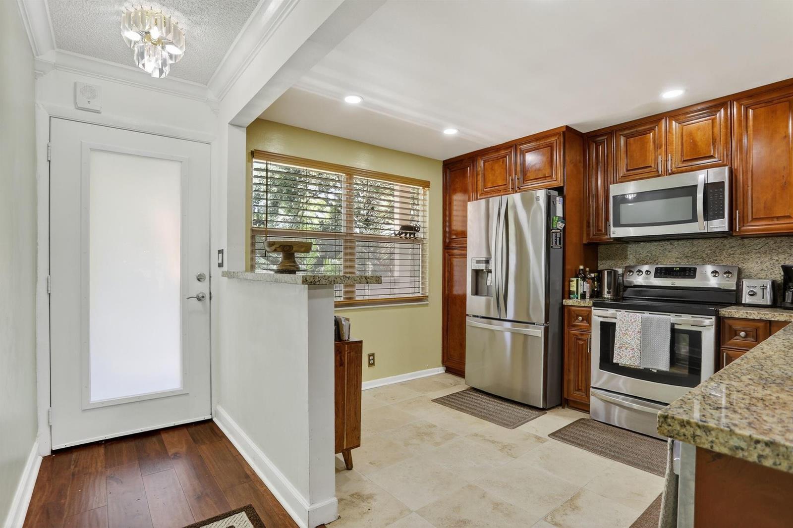 A kitchen features stainless steel appliances, wood cabinetry, granite countertops, and a tile floor — 2403 Antigua Circle # B2, Coconut Creek FL 33066, COCONUT CREEK, FL