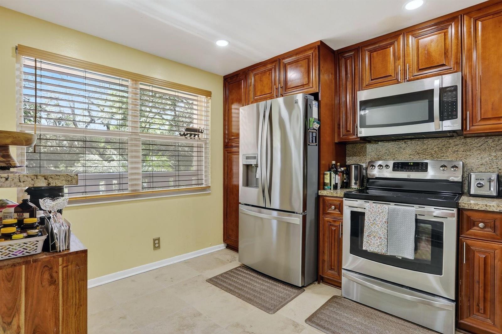 A kitchen features stainless steel appliances, dark wood cabinetry, granite countertops, and a large window — 2403 Antigua Circle # B2, Coconut Creek FL 33066, COCONUT CREEK, FL
