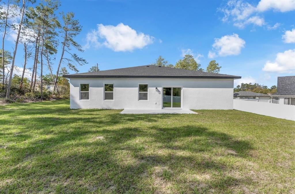 The rear exterior of a white single-story house with a concrete patio and grassy yard — 4411 SW 172ND ST ROAD, OCALA, FL