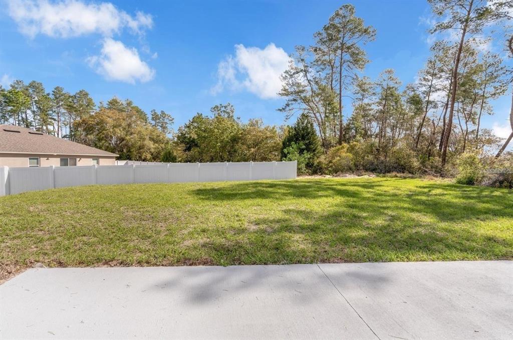 A grassy backyard with a white vinyl fence and trees under a blue sky — 4411 SW 172ND ST ROAD, OCALA, FL
