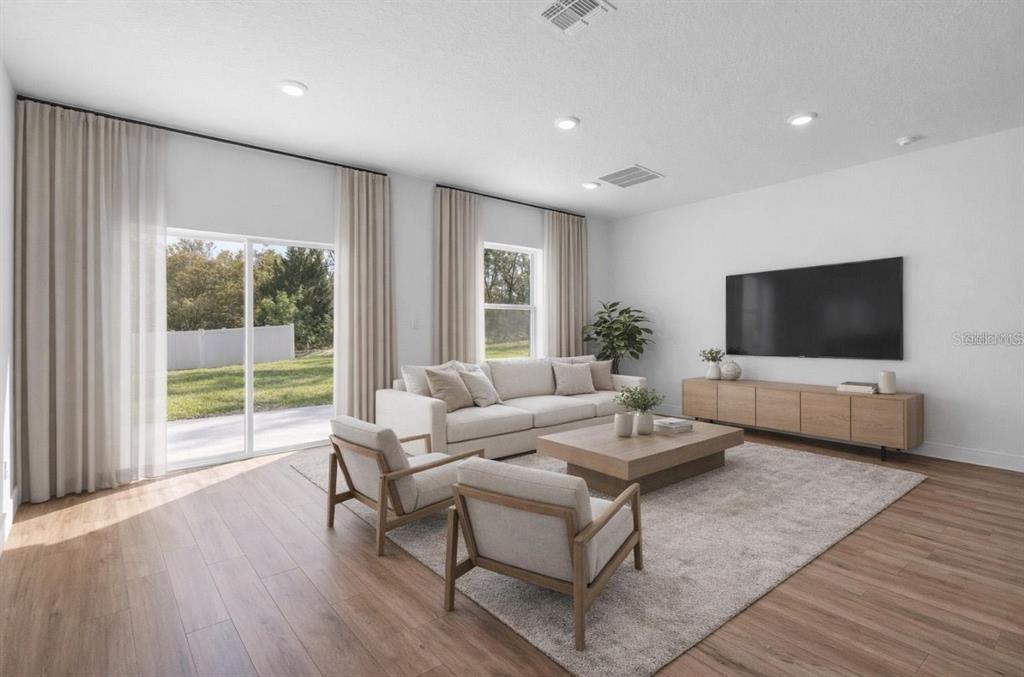 A living room with light wood flooring, a beige sofa, two armchairs, and a television — 4411 SW 172ND ST ROAD, OCALA, FL