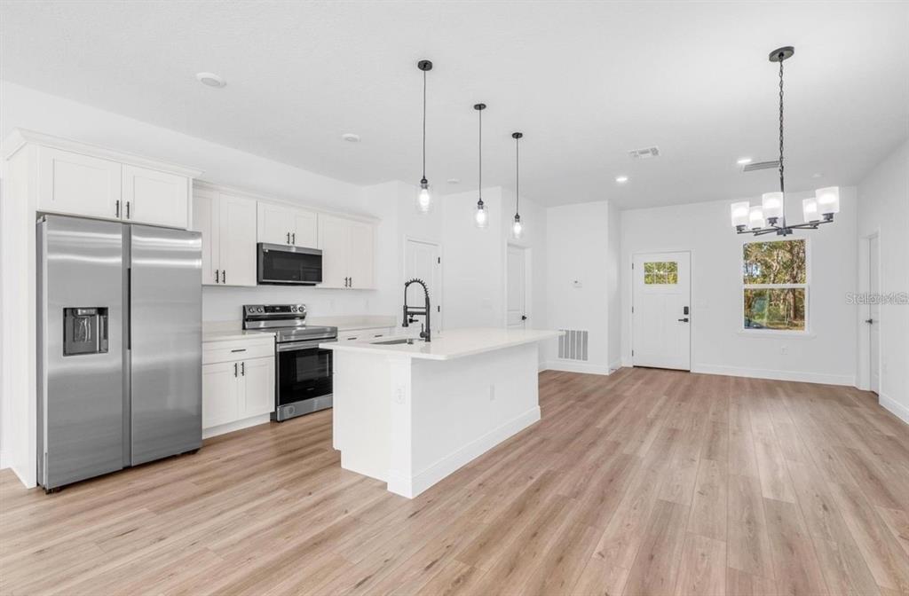A modern kitchen features white cabinetry, stainless steel appliances, a center island, and wood flooring — 4411 SW 172ND ST ROAD, OCALA, FL