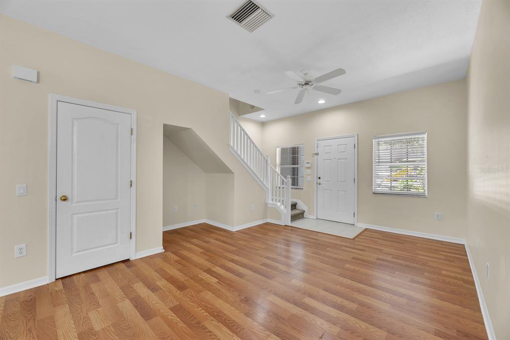 An empty room with wood-look flooring, a white staircase, and a front entry door — 6737 LAKE ROCHESTER LANE, GIBSONTON, FL