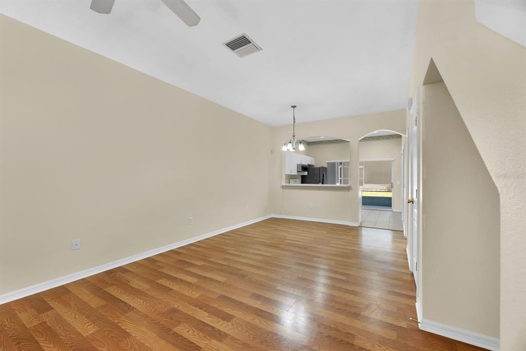 An empty room with wood-look flooring, beige walls, and an opening to a kitchen area — 6737 LAKE ROCHESTER LANE, GIBSONTON, FL