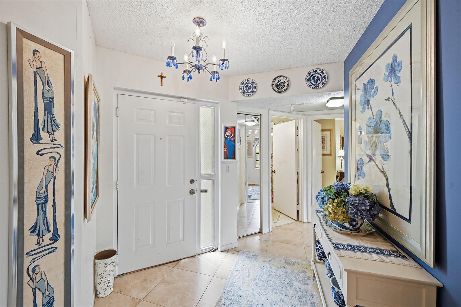 A bright entryway features a blue-and-white chandelier, tiled floors, and blue-accented wall decor — 5442 Firenze Drive # F, Boynton Beach FL 33437, BOYNTON BEACH, FL