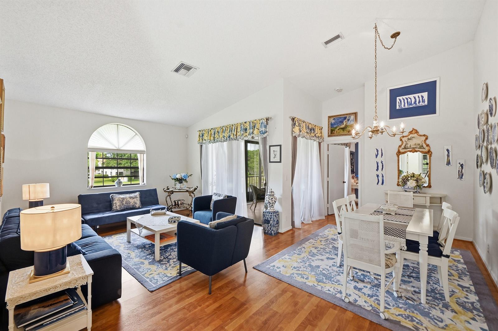 A bright living and dining area features blue furniture, hardwood floors, and large arched windows — 5442 Firenze Drive # F, Boynton Beach FL 33437, BOYNTON BEACH, FL