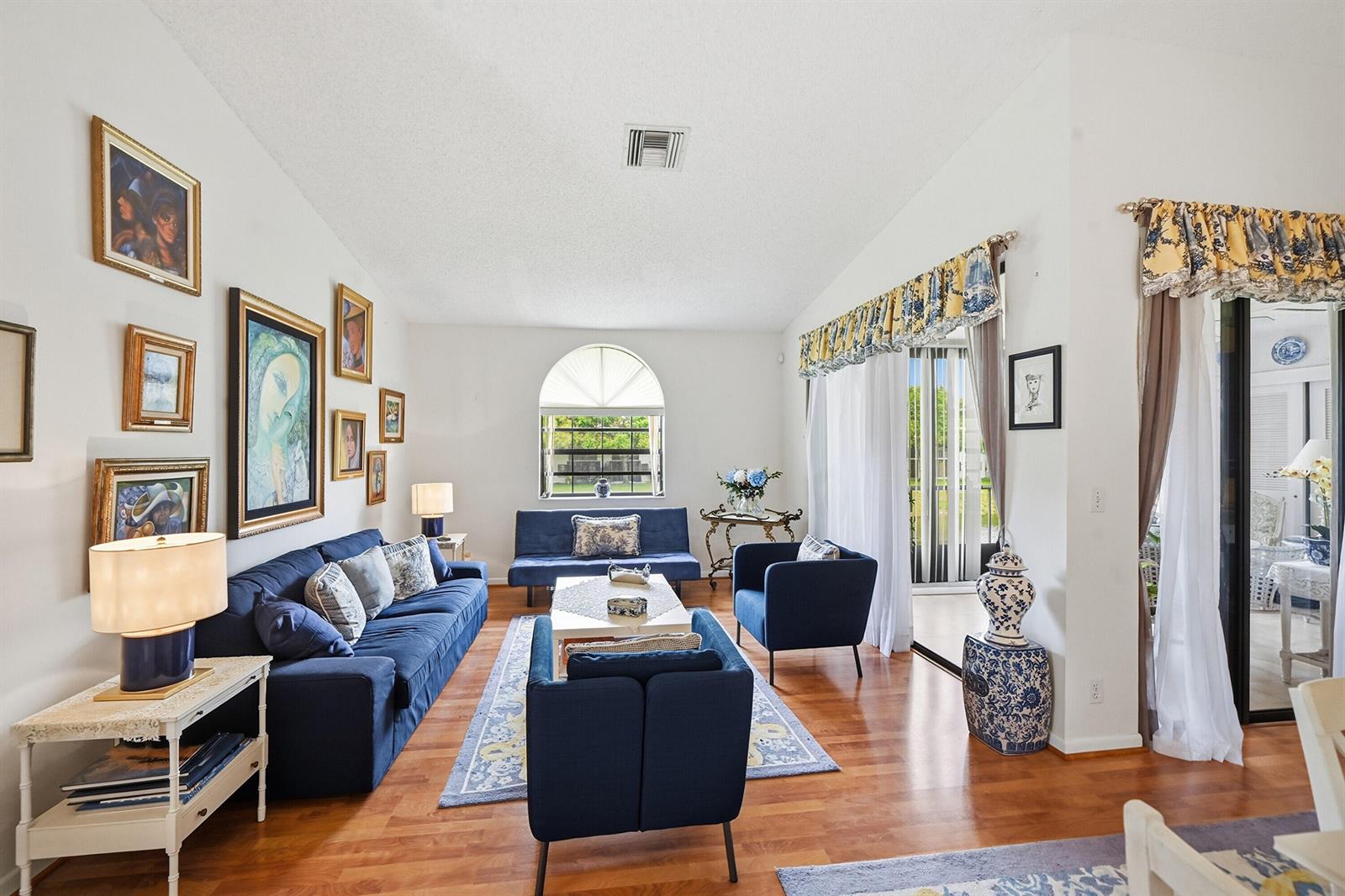 A living room features blue sofas, hardwood floors, a gallery wall, and large sliding glass doors — 5442 Firenze Drive # F, Boynton Beach FL 33437, BOYNTON BEACH, FL