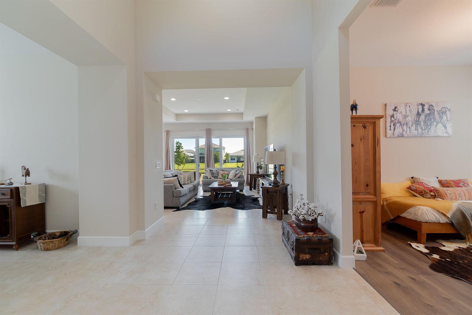 A tiled hallway leads to a living room with large windows and an adjacent bedroom — 4644 Citron Way, Westlake FL 33470, WESTLAKE, FL