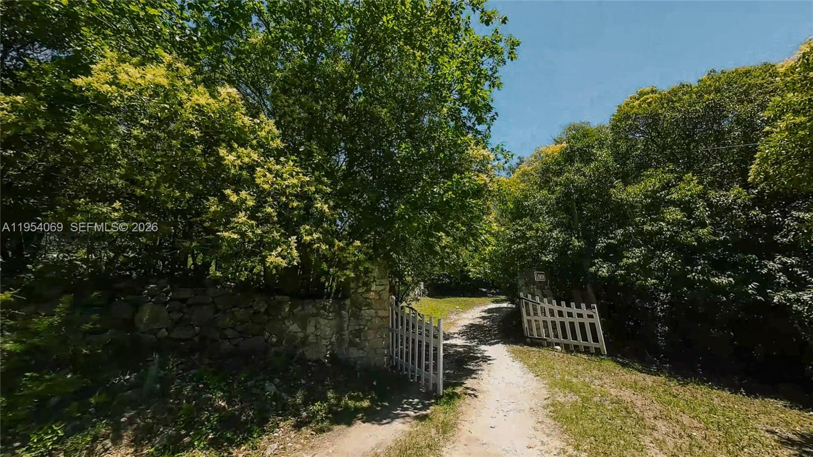 A dirt path leads through an open white gate flanked by stone walls and trees — 1 Segundo Paredon, ALTA GRACIA, 5186, FL