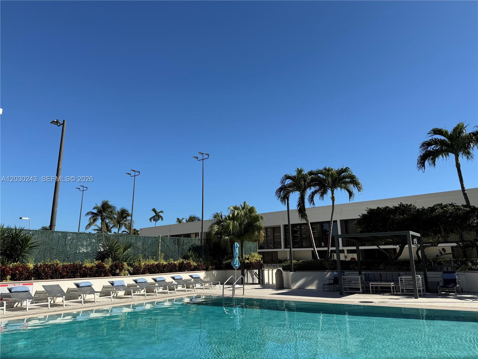 A swimming pool with lounge chairs and palm trees sits in front of a building — 1925 Brickell Ave # 1403, Miami FL 33129, MIAMI, FL