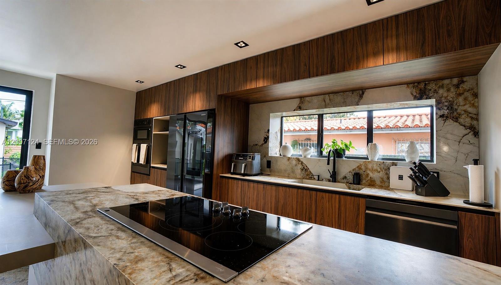 A modern kitchen features wood cabinetry, a marble island with a cooktop, and stone backsplash — 1820 SW 10th St, Miami FL 33135, MIAMI, FL