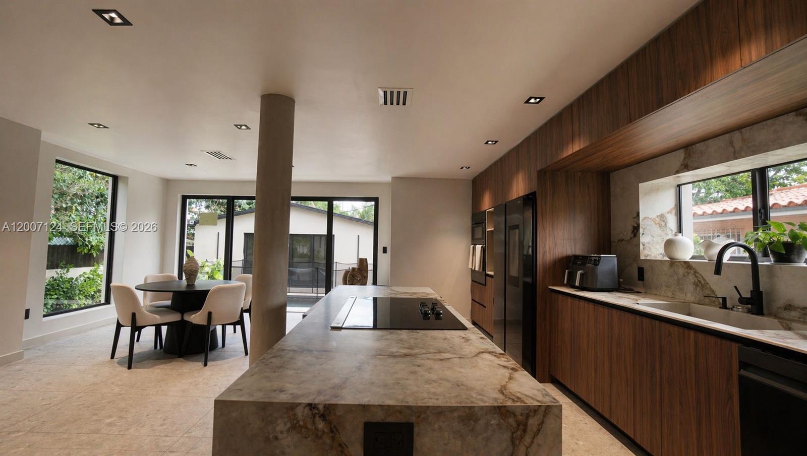 A modern kitchen features a large stone island, wood cabinetry, and a dining area nearby — 1820 SW 10th St, Miami FL 33135, MIAMI, FL