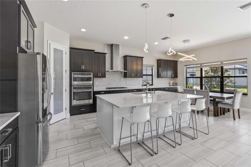 A modern kitchen features dark cabinetry, a white quartz island with bar seating, and stainless appliances — 805 VISCOUNT STREET, BRANDON, FL