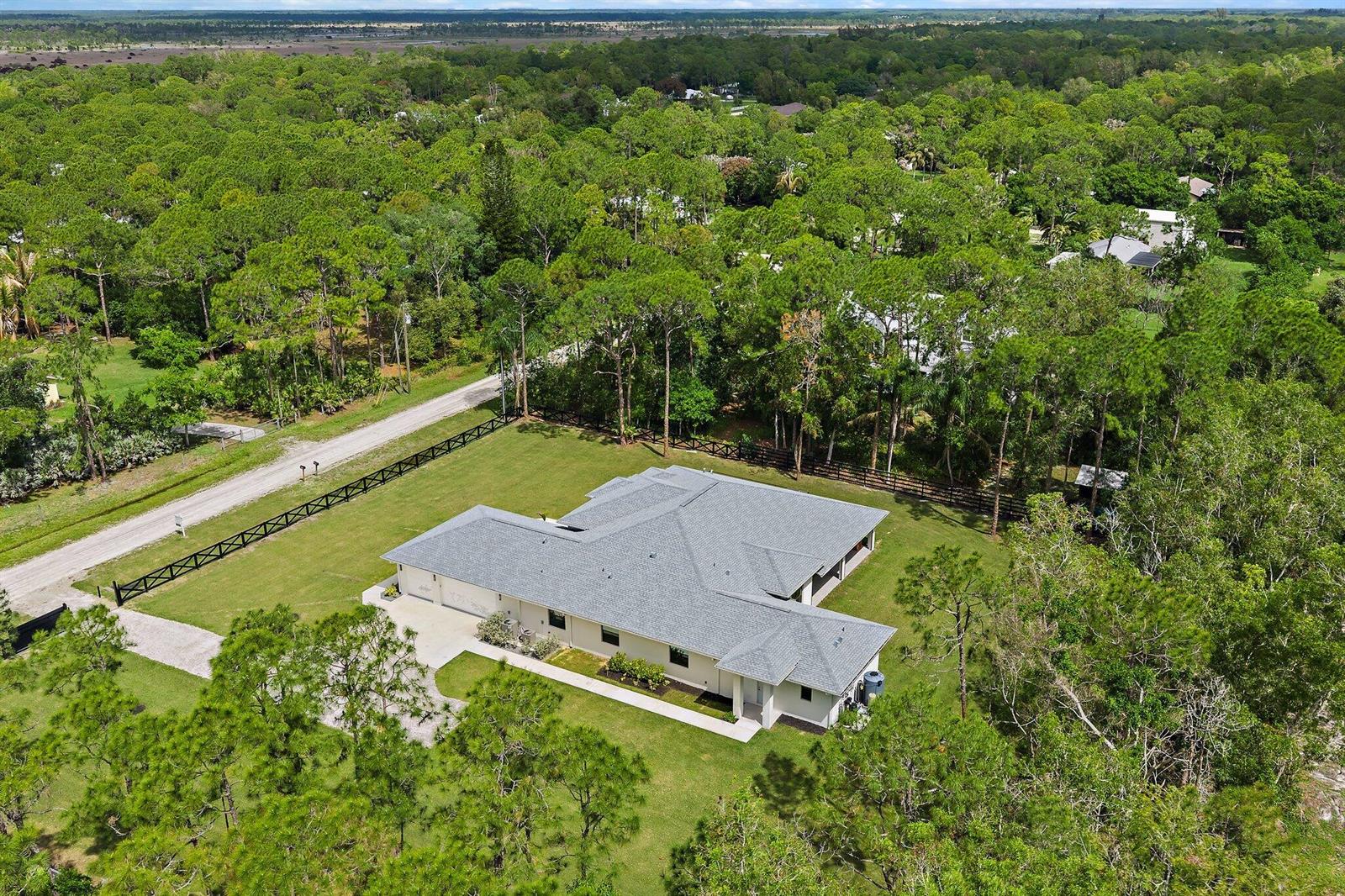 An aerial view shows a single-story house with a gray roof surrounded by wooded land — 16096 132nd Terrace N, Jupiter FL 33478, JUPITER, FL