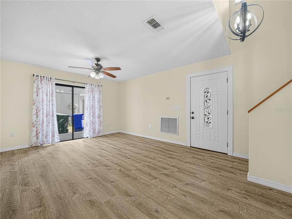 A living room features wood-look flooring, a ceiling fan, a sliding glass door, and an entryway — 3573 RAINTREE CIRCLE, LAKELAND, FL