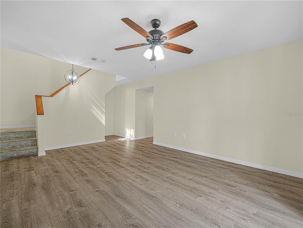 An empty living room features wood-look flooring, a ceiling fan, and a staircase — 3573 RAINTREE CIRCLE, LAKELAND, FL