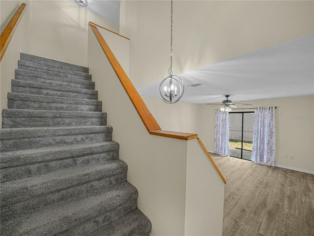 A carpeted staircase with a wooden handrail overlooks a living area with wood-look flooring — 3573 RAINTREE CIRCLE, LAKELAND, FL