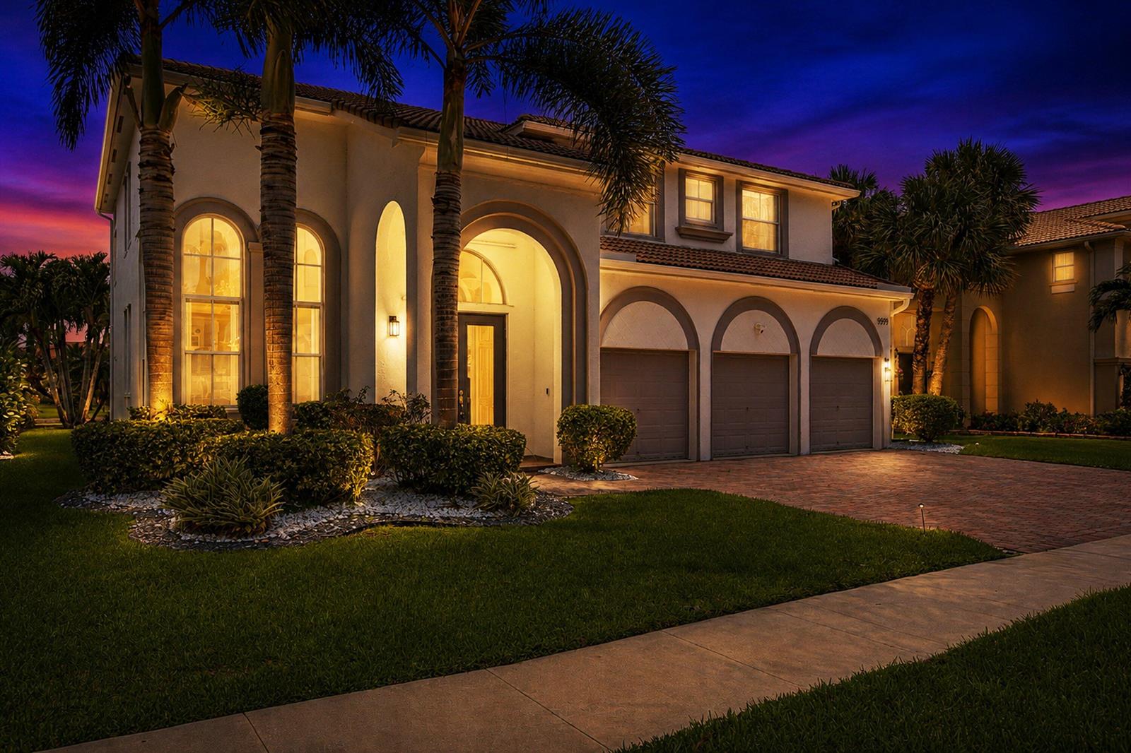 A two-story house with a three-car garage and arched windows at dusk — 9599 Shepard Place, Wellington FL 33414, WELLINGTON, FL
