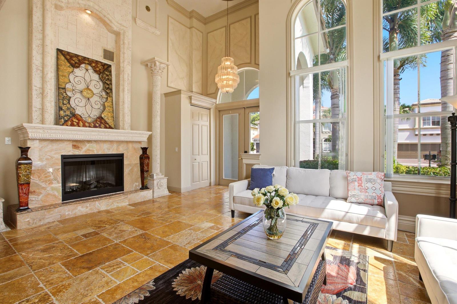 A high-ceilinged living room features a stone fireplace, tile flooring, and large arched windows — 9599 Shepard Place, Wellington FL 33414, WELLINGTON, FL