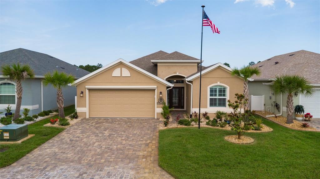 A tan single-story house with a paved driveway, a front lawn, and an American flag — 37 LAGOON WAY, PALM COAST, FL