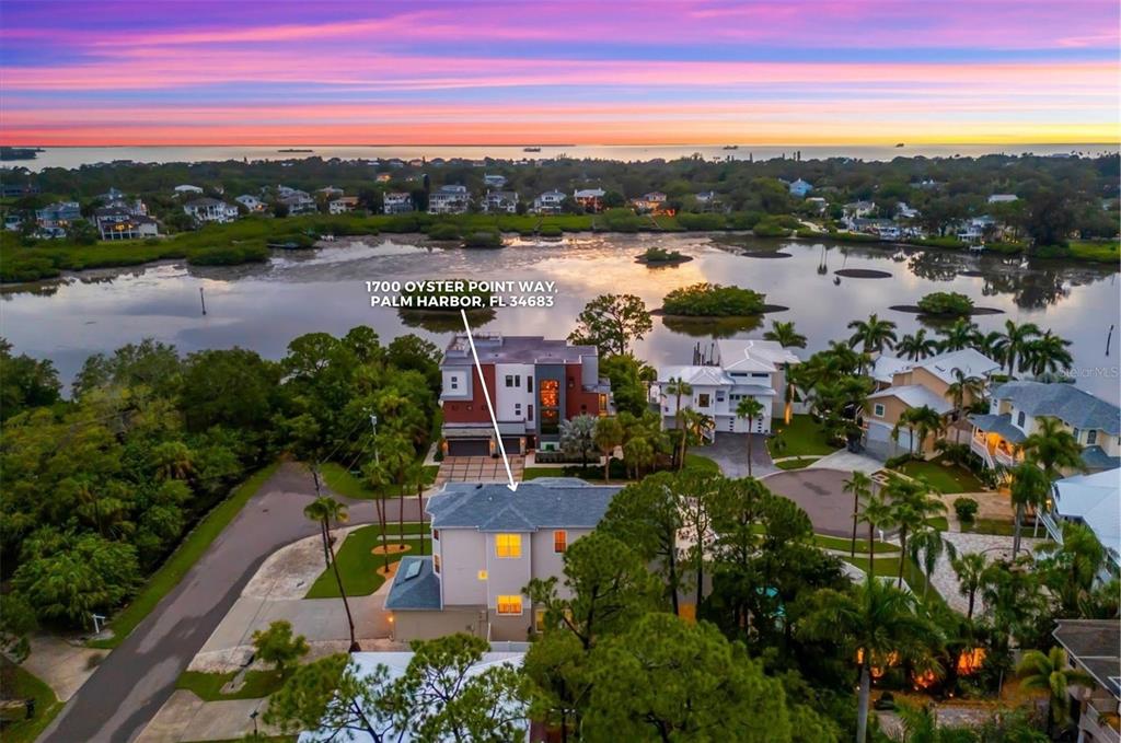 An aerial view shows a multi-story house near a bay at sunset — 1700 OYSTER POINT WAY, PALM HARBOR, FL