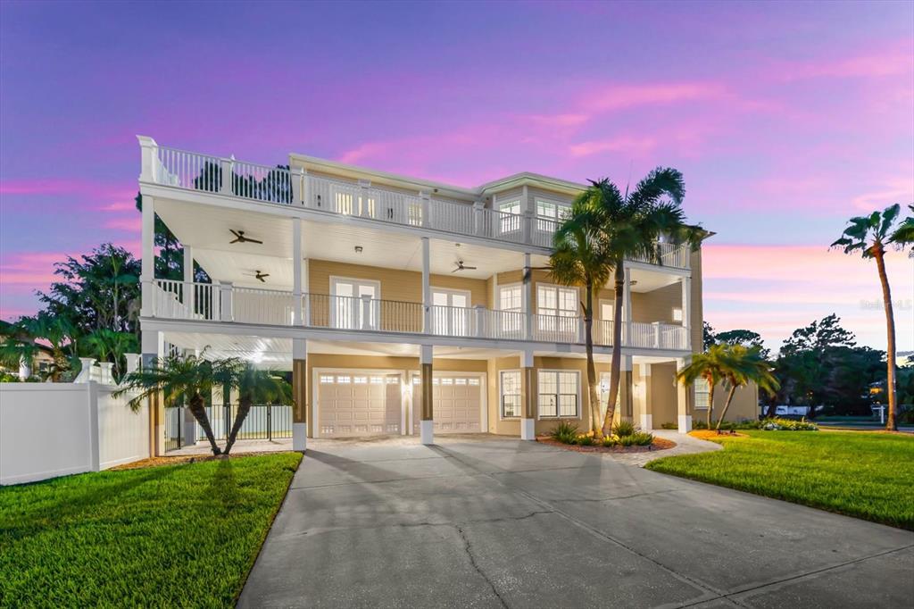 A three-story house with a beige exterior, a concrete driveway, and a large palm tree — 1700 OYSTER POINT WAY, PALM HARBOR, FL